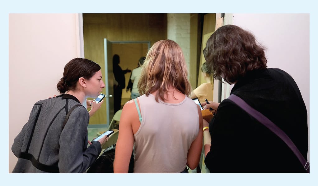 Audience members in Project Amelia act as journalist characters and peer at their phones.